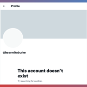 A screenshot displaying a social media profile error message. The profile header shows a placeholder for a profile picture and the username "@hearmikeburke." Below the username, a bold message states "This account doesn’t exist" followed by a suggestion to "Try searching for another." The background gradient transitions from red to blue, indicating a possible error or inactive status on the social media platform.